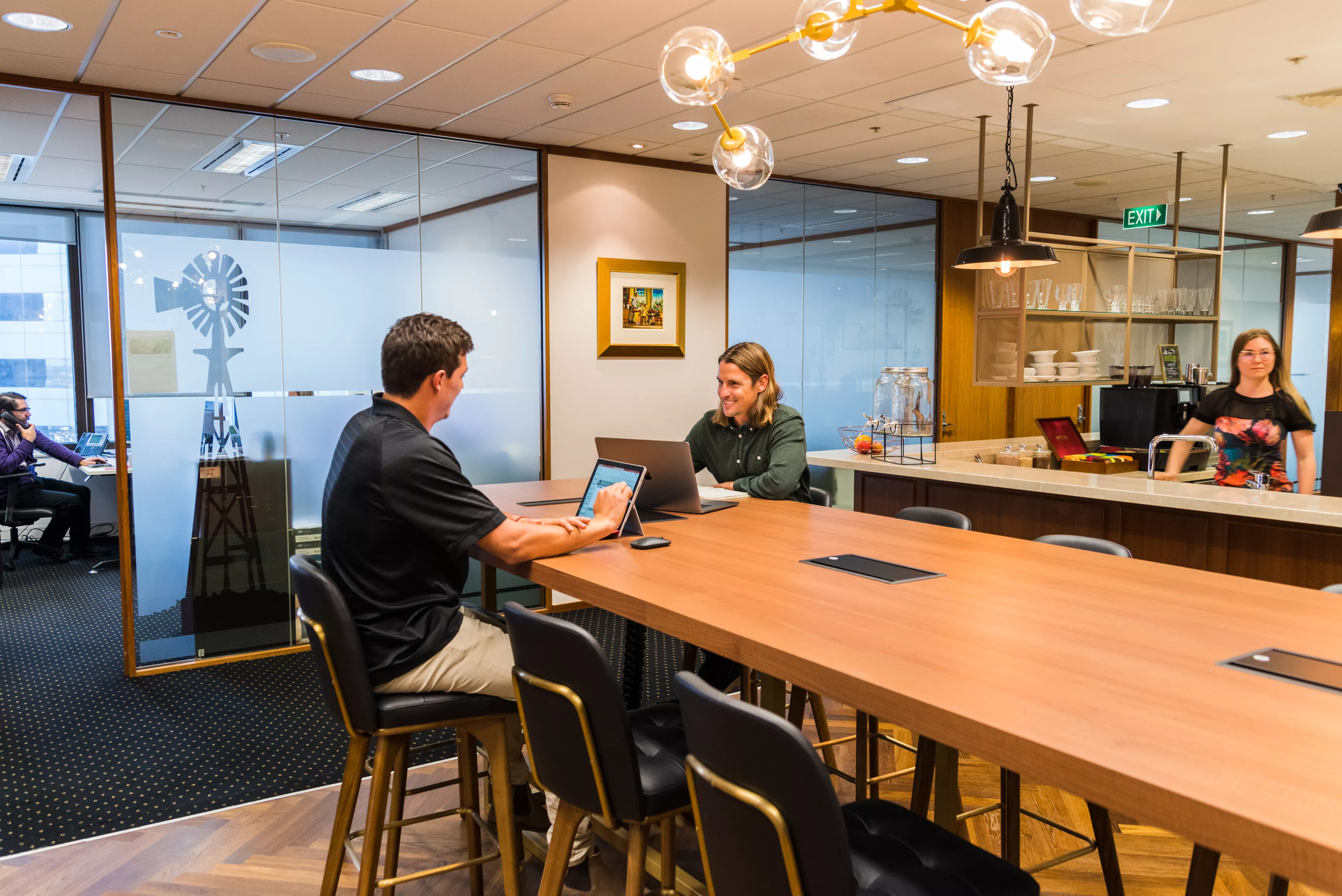 Clients working in a modern coworking space on a large table, enjoying the fully stocked kitchen in Servcorp 140 St Georges Terrace Perth