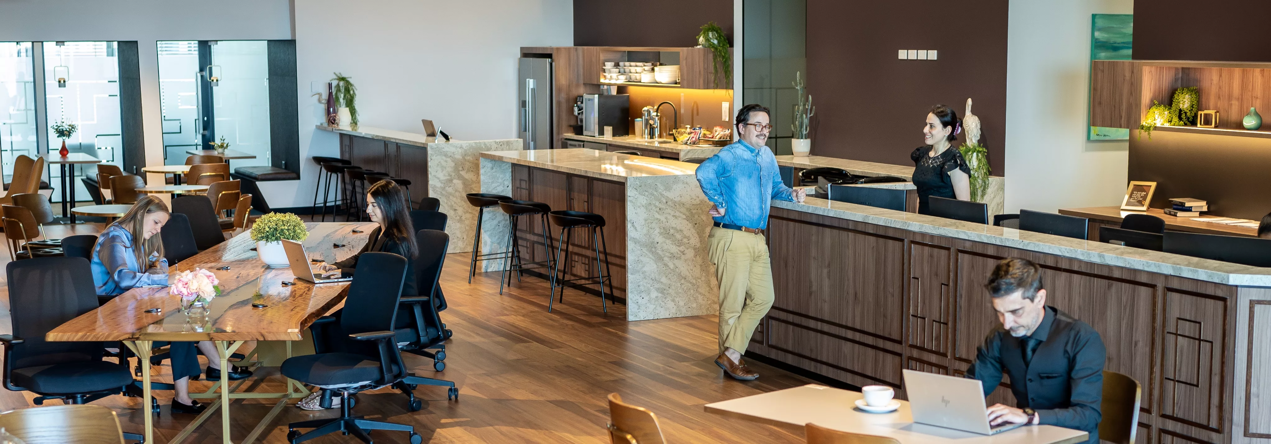 Clients working in a modern coworking space with a kitchen lounge and a receptionist helping a client in Servcorp 100 Mount Street